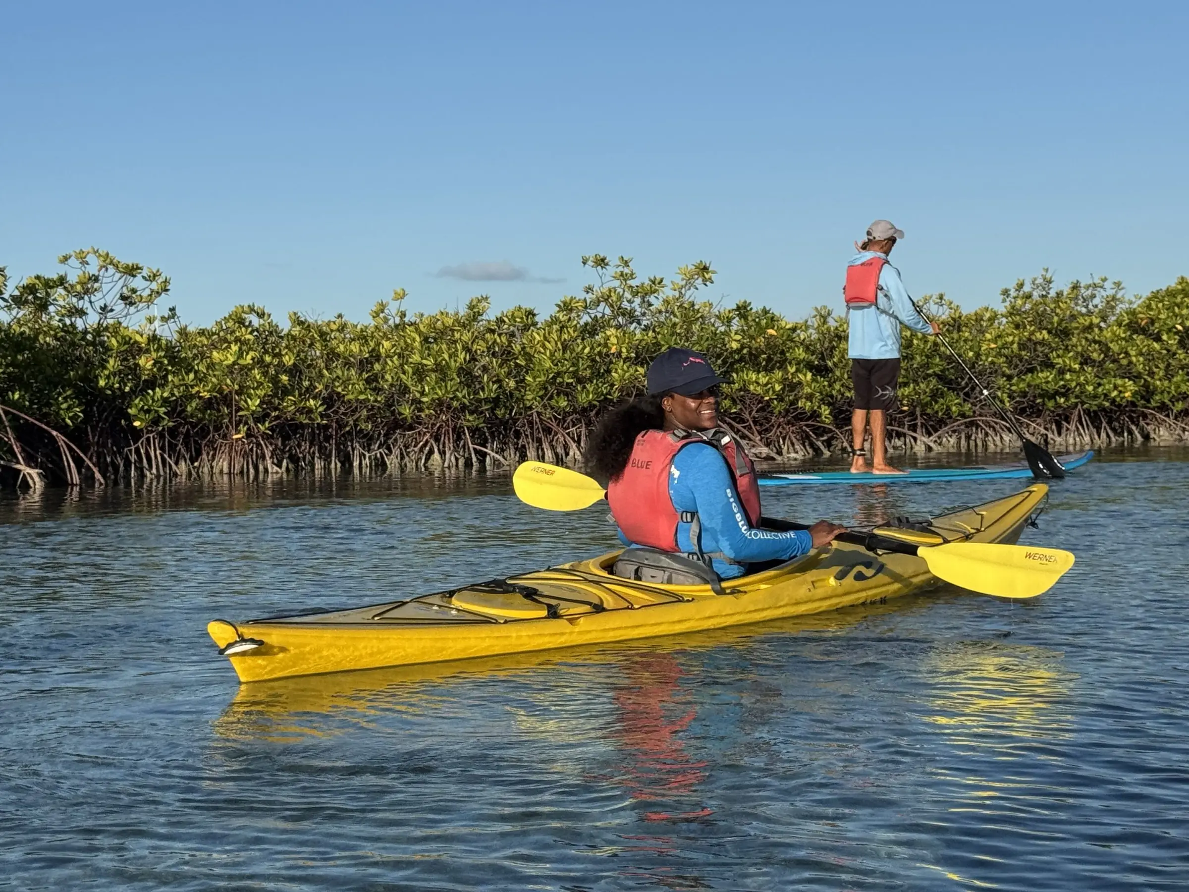 A guide on a paddleboard beside guests in a yellow kayak