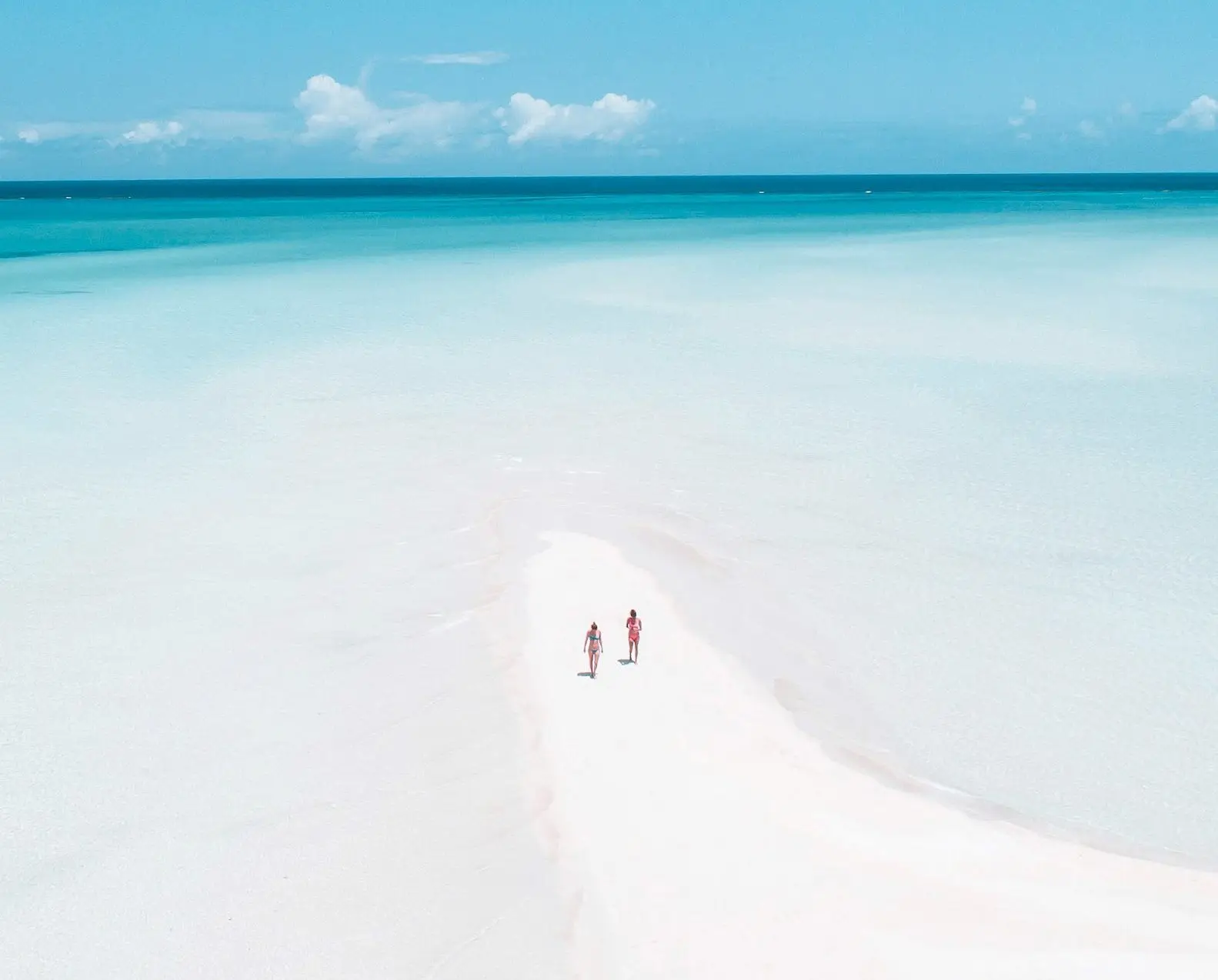 Two people on a white sandbar in pale blue water at low tide
