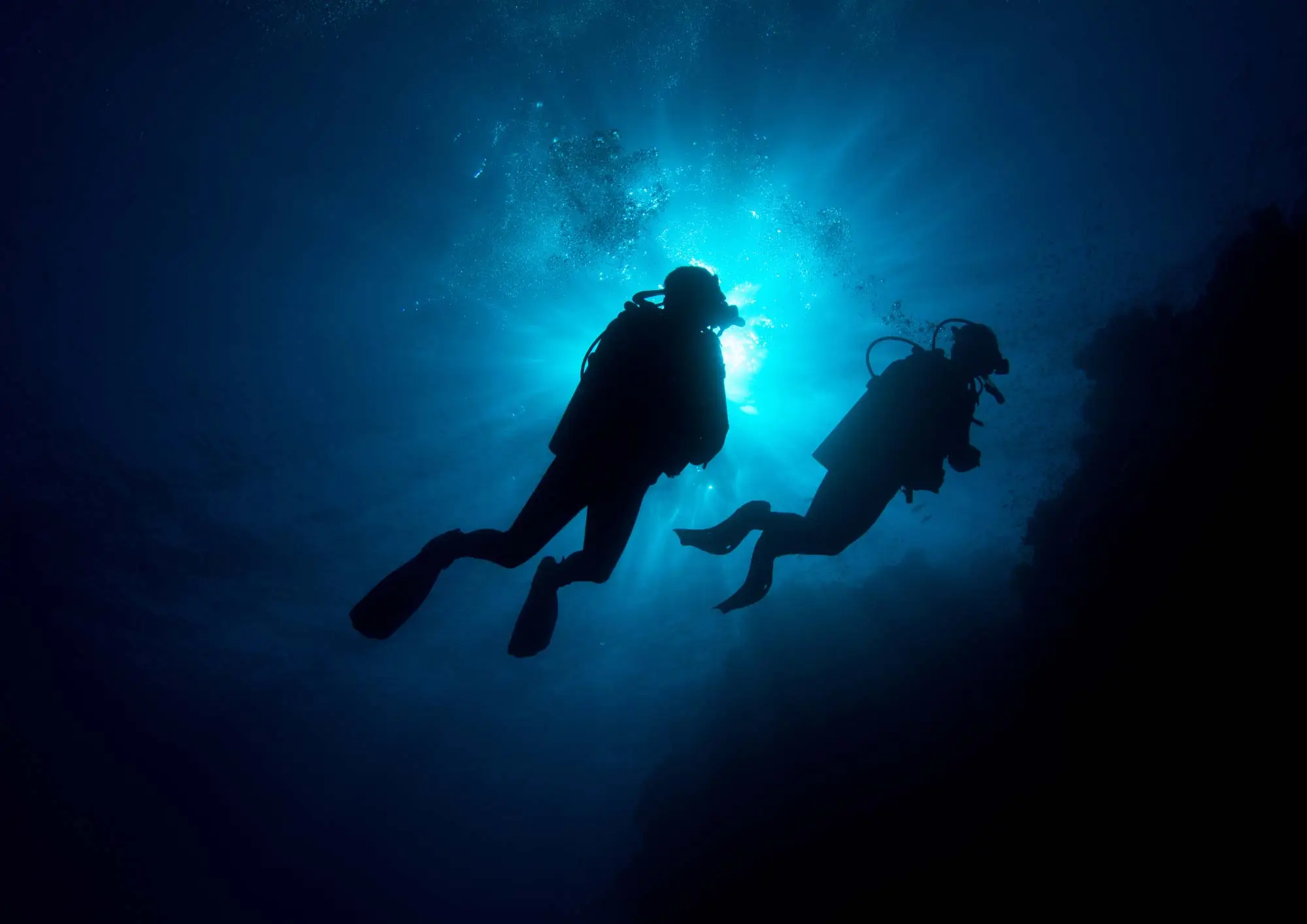 Two scuba divers silhouetted against sunlight in deep blue water
