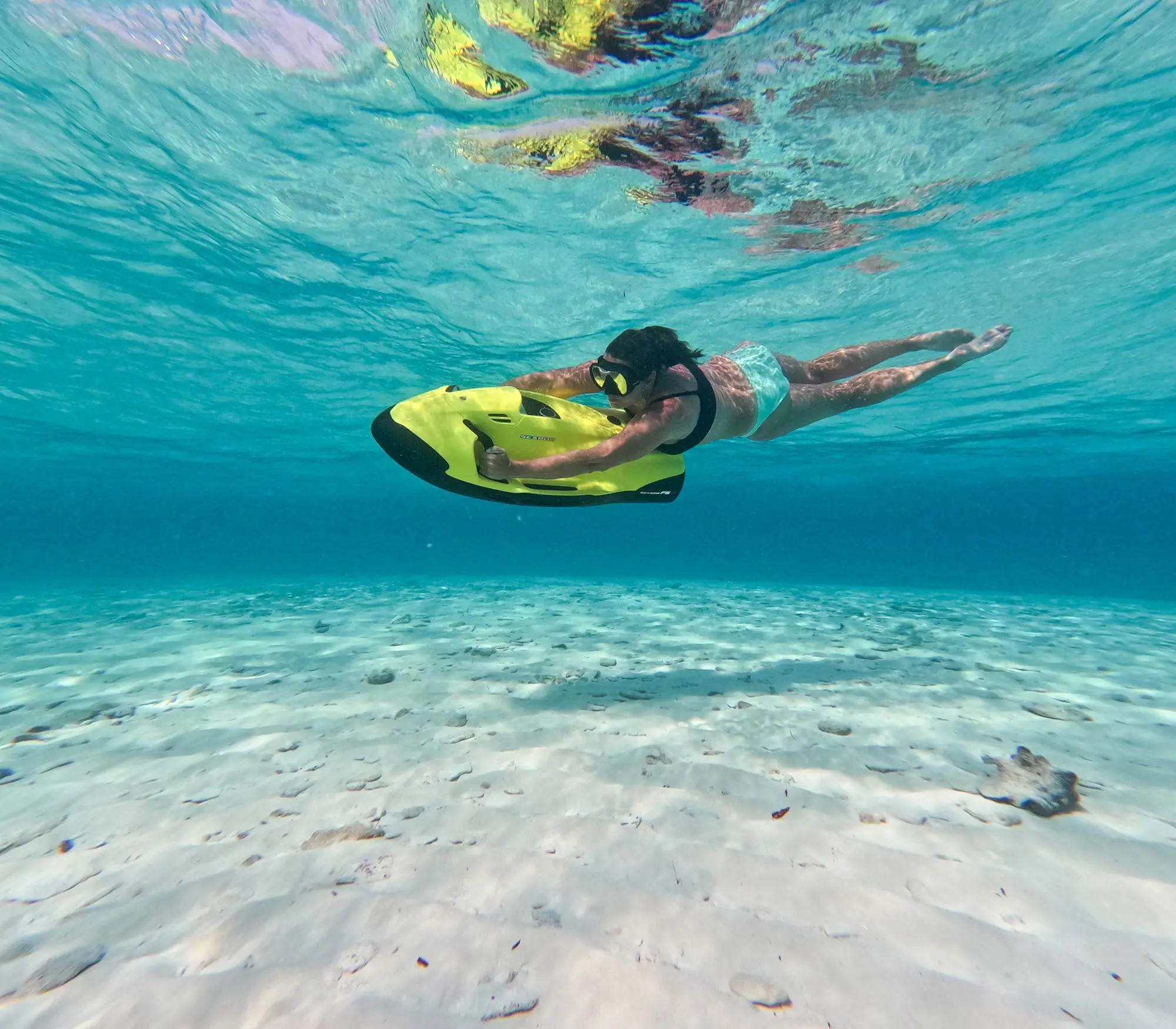Snorkeler riding a yellow Seabob underwater scooter over white sand